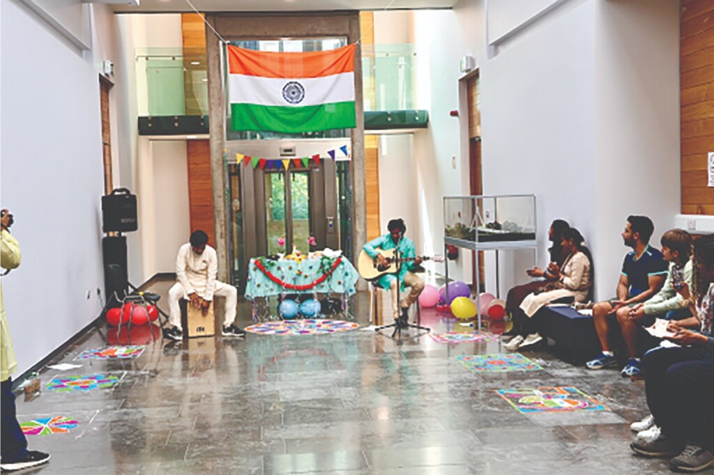 Indian staff and students performing Indian music in traditional Indian attire; the Rangoli art form is showcased on the floor.